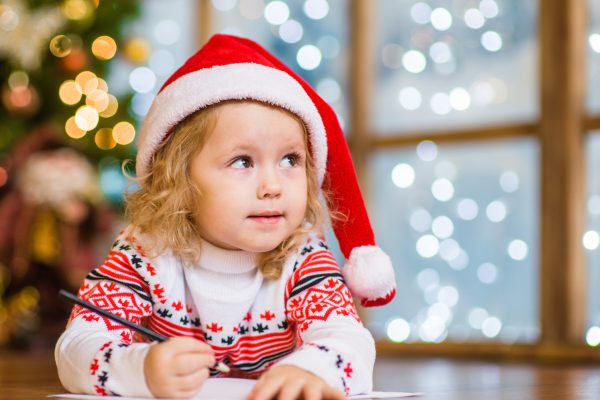 Little girl in red christmas hat writes letter to Santa Claus.