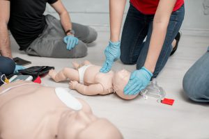First aid training Instructor showing how to make chest compressions on a baby dummy during the first aid training indoors