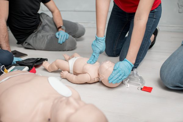 Instructor showing how to make chest compressions on a baby dummy during the first aid training indoors