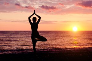 Woman at sunset practicing yoga. Seashore, silhouette