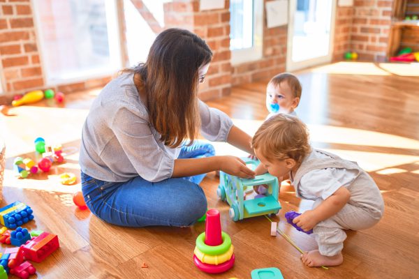 Beautiful teacher and toddlers playing around lots of toys at kindergarten