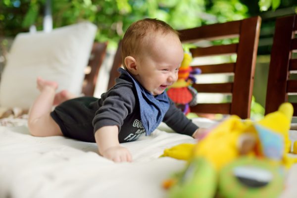 Cute three months old baby boy playing with his colourful toys outdoor. Baby during tummy time. Cute little child learning to crawl.