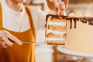 Caucasian pastry chef woman showing piece of cake with chocolate cream indoors