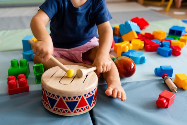 Little boy having fun and playing wooden toy drum