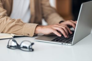 Close up of a mans hands typing on a laptop keyboard.